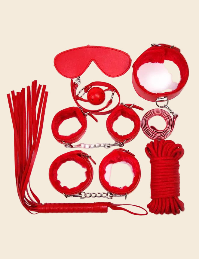 A collection of red bondage accessories including a ball gag, wrist cuffs, ankle cuffs, a collar with leash, a whip, an eye mask, and a roll of rope.