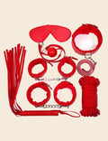 A collection of red bondage accessories including a ball gag, wrist cuffs, ankle cuffs, a collar with leash, a whip, an eye mask, and a roll of rope.
